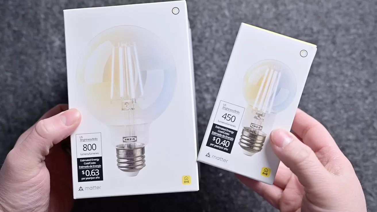 Two hands holding two white LED light bulb boxes of different sizes, showing wattage and brightness labels, against a gray textured background