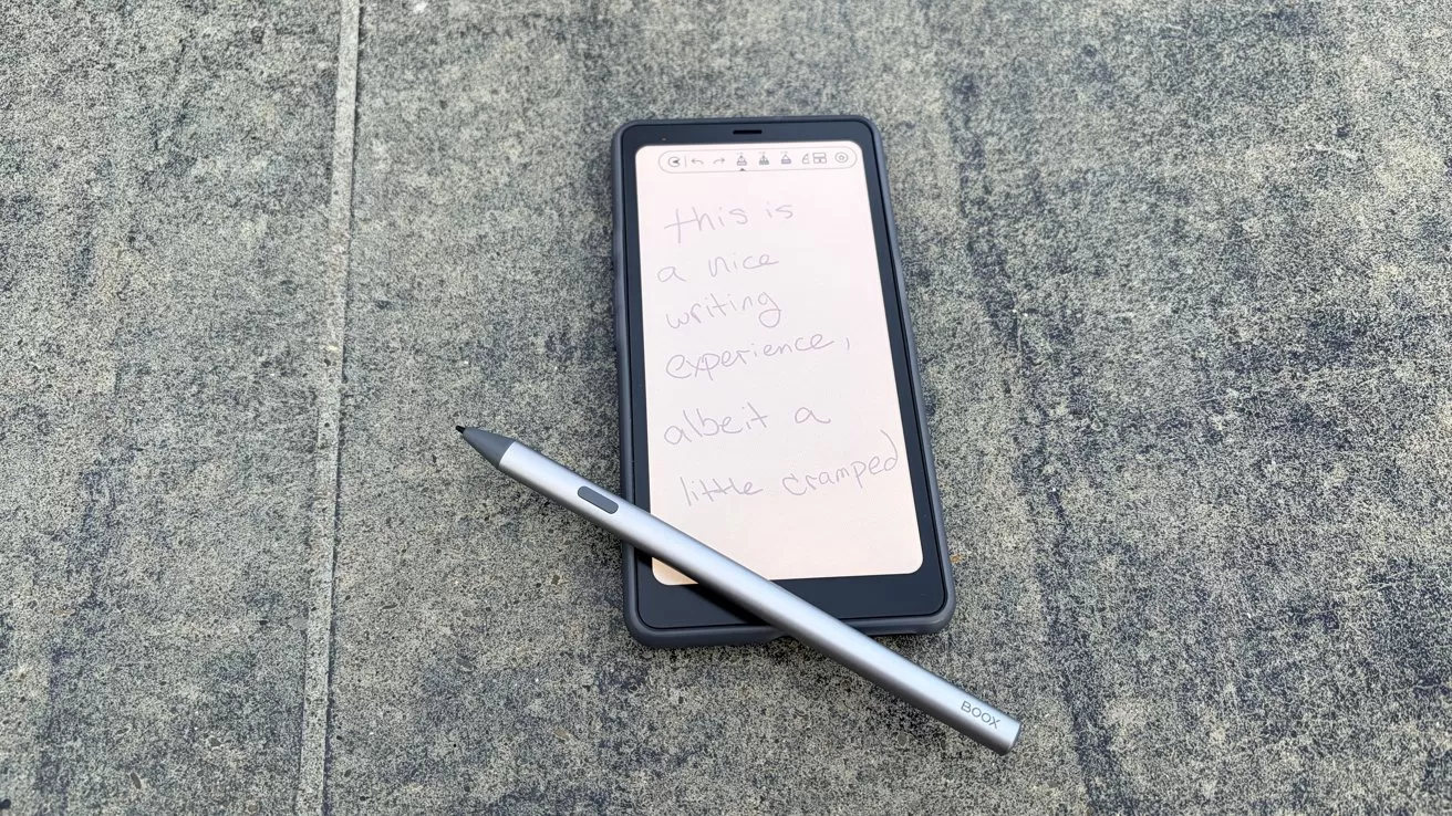 Smartphone with handwritten note on screen, placed on concrete surface, accompanied by a silver stylus.