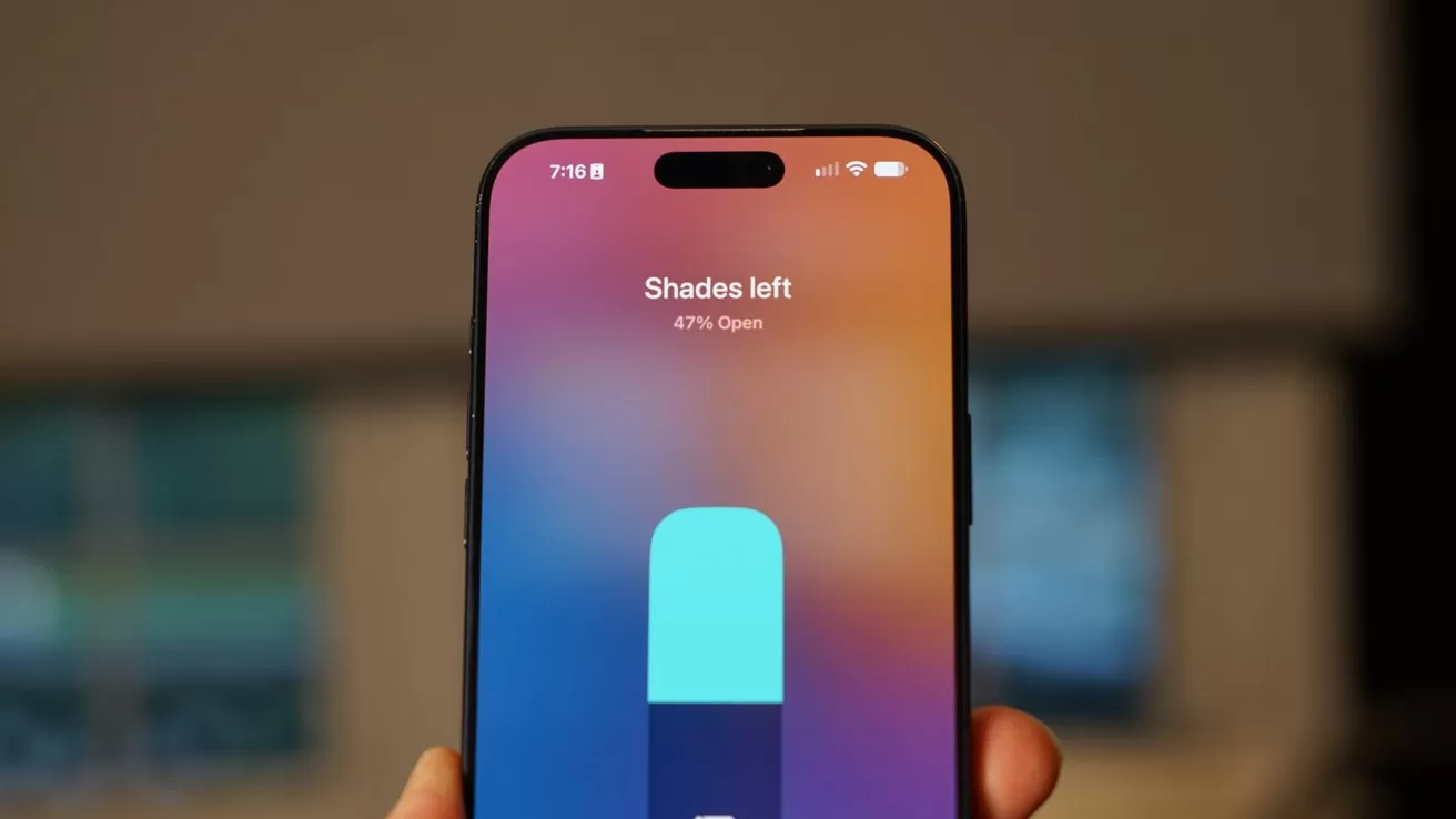 Hand holding a smartphone displaying a colorful gradient screen with a large vertical control slider labeled Shades left at 47 percent open, against a softly blurred indoor background