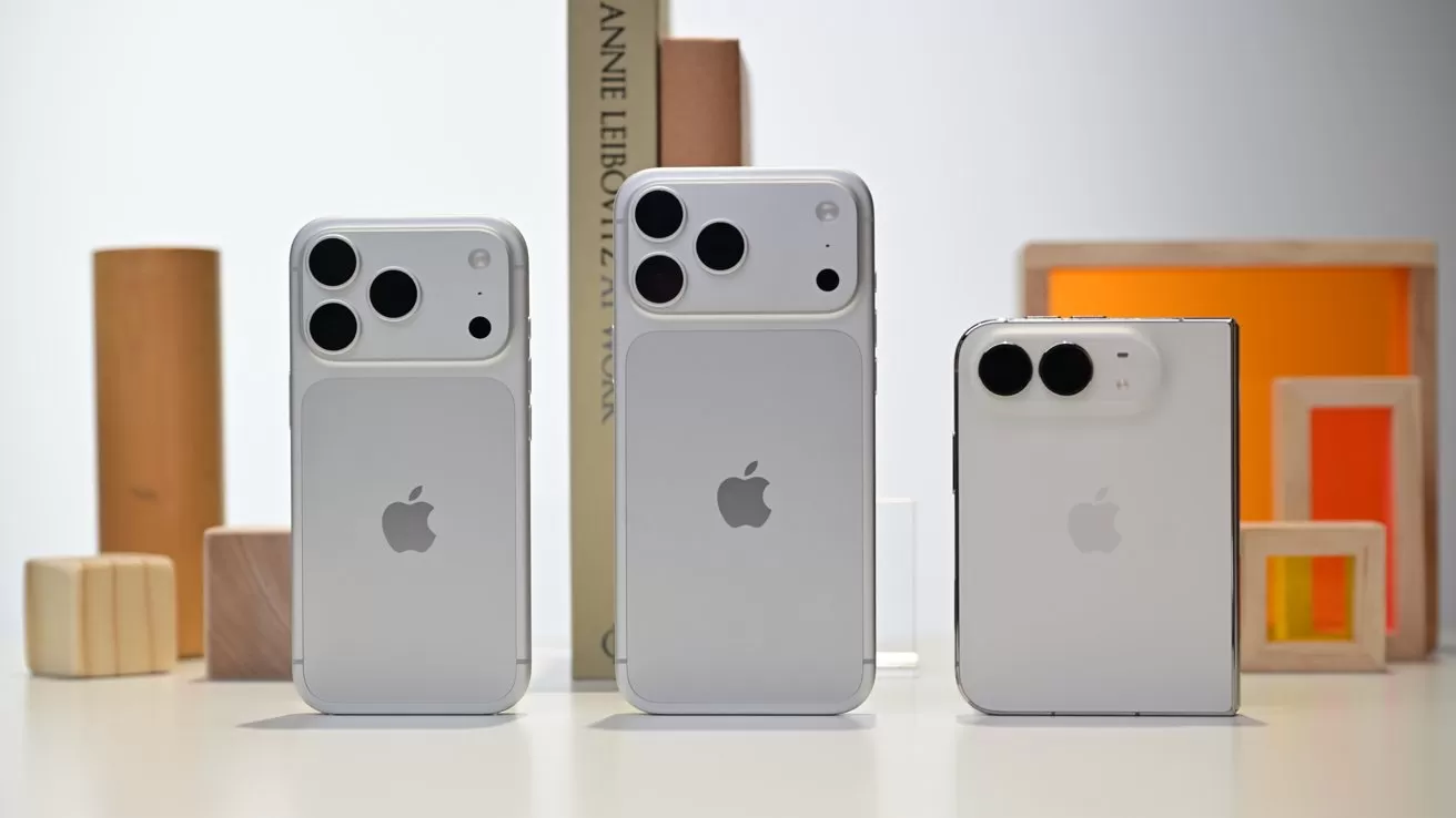 Three silver iPhones with large rear cameras stand upright on a white surface, surrounded by minimal wooden blocks and colorful geometric frames in a softly lit, modern setting