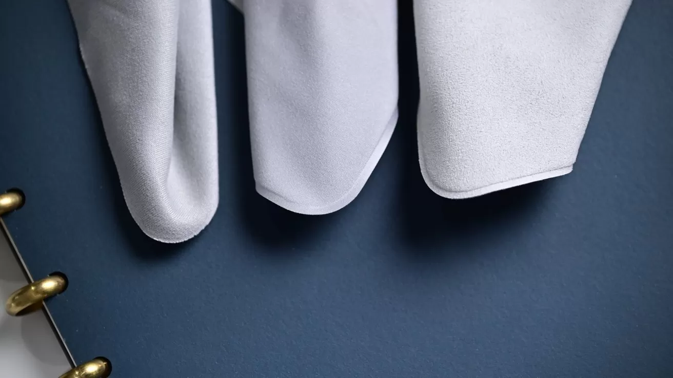 Close view of three white glove fingers resting on a dark blue surface, with part of a gold metal ring binder visible along the left edge