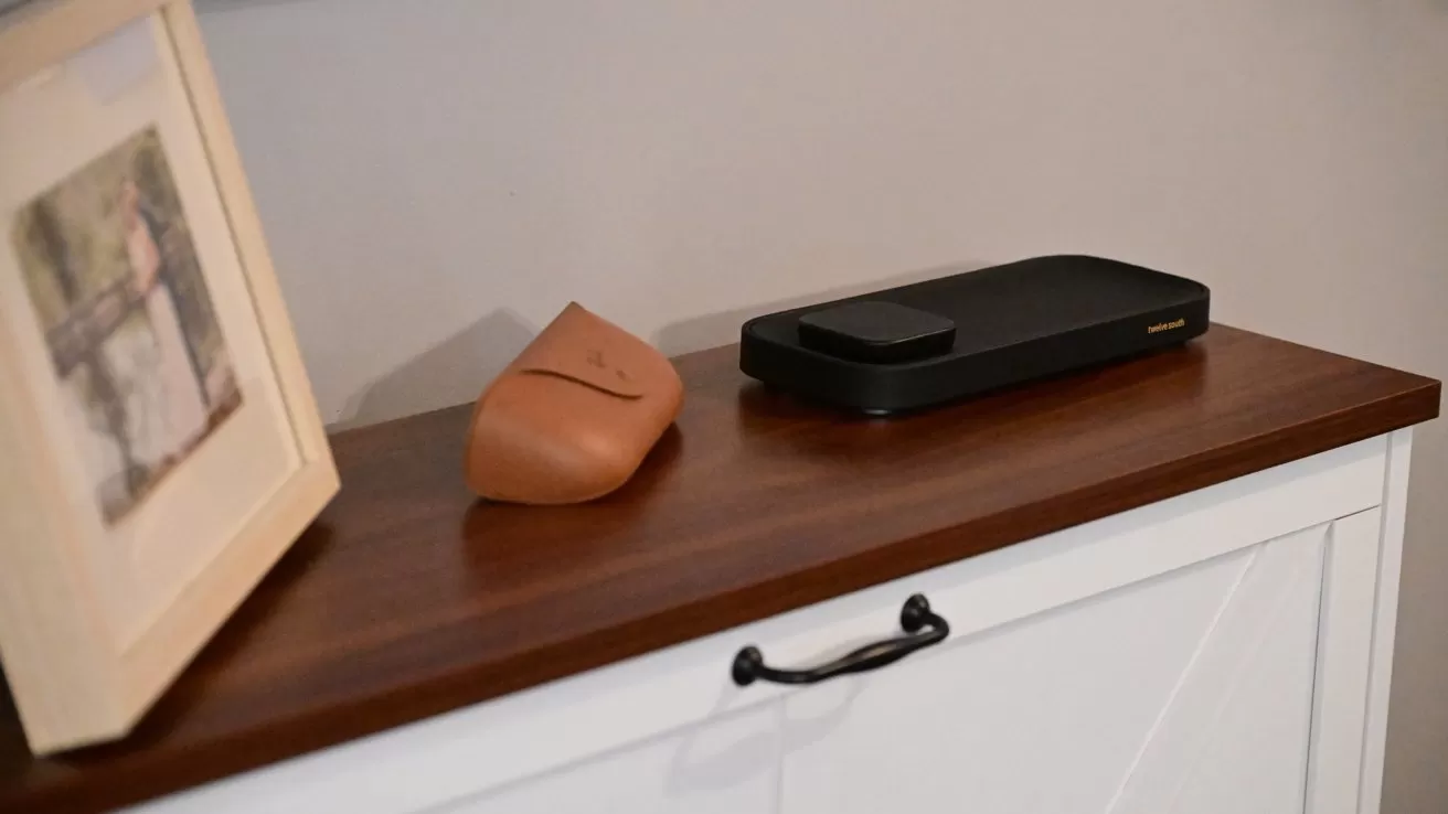 Wooden cabinet top with framed photo, small tan leather case, and a slim black electronic device, against a plain light-colored wall in a tidy, modern room