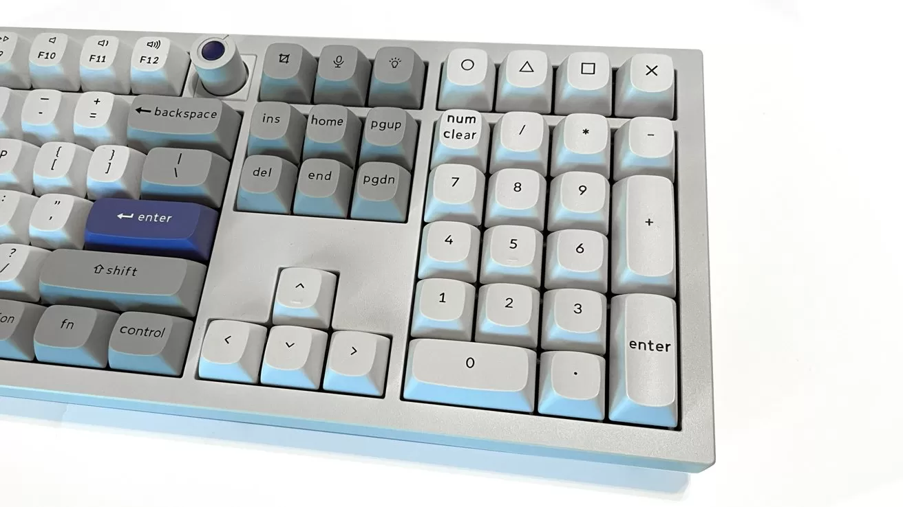 Close-up of a light gray mechanical keyboard showing number pad, navigation keys, and a few dark blue keys, on a white background