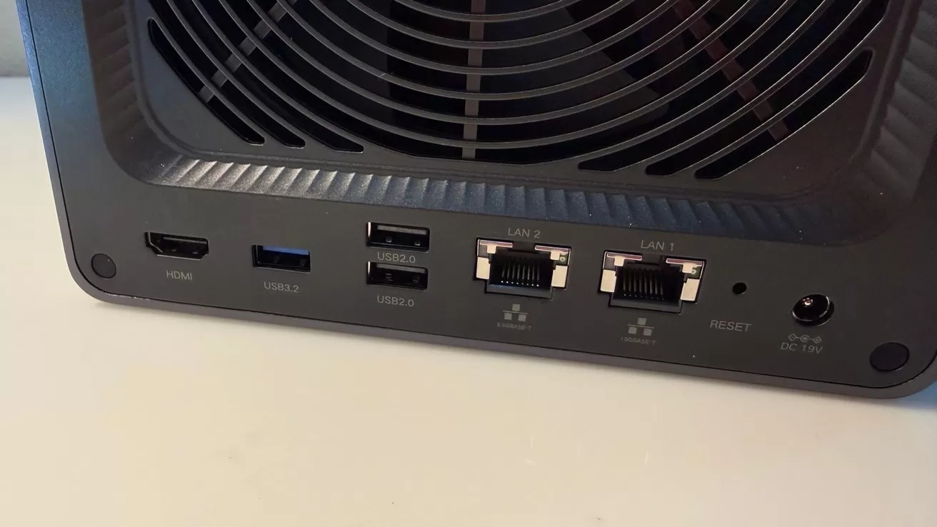 Back panel of a network device showing a large cooling fan, HDMI port, USB ports, two Ethernet LAN ports, a reset button, and a round power connector on a white surface