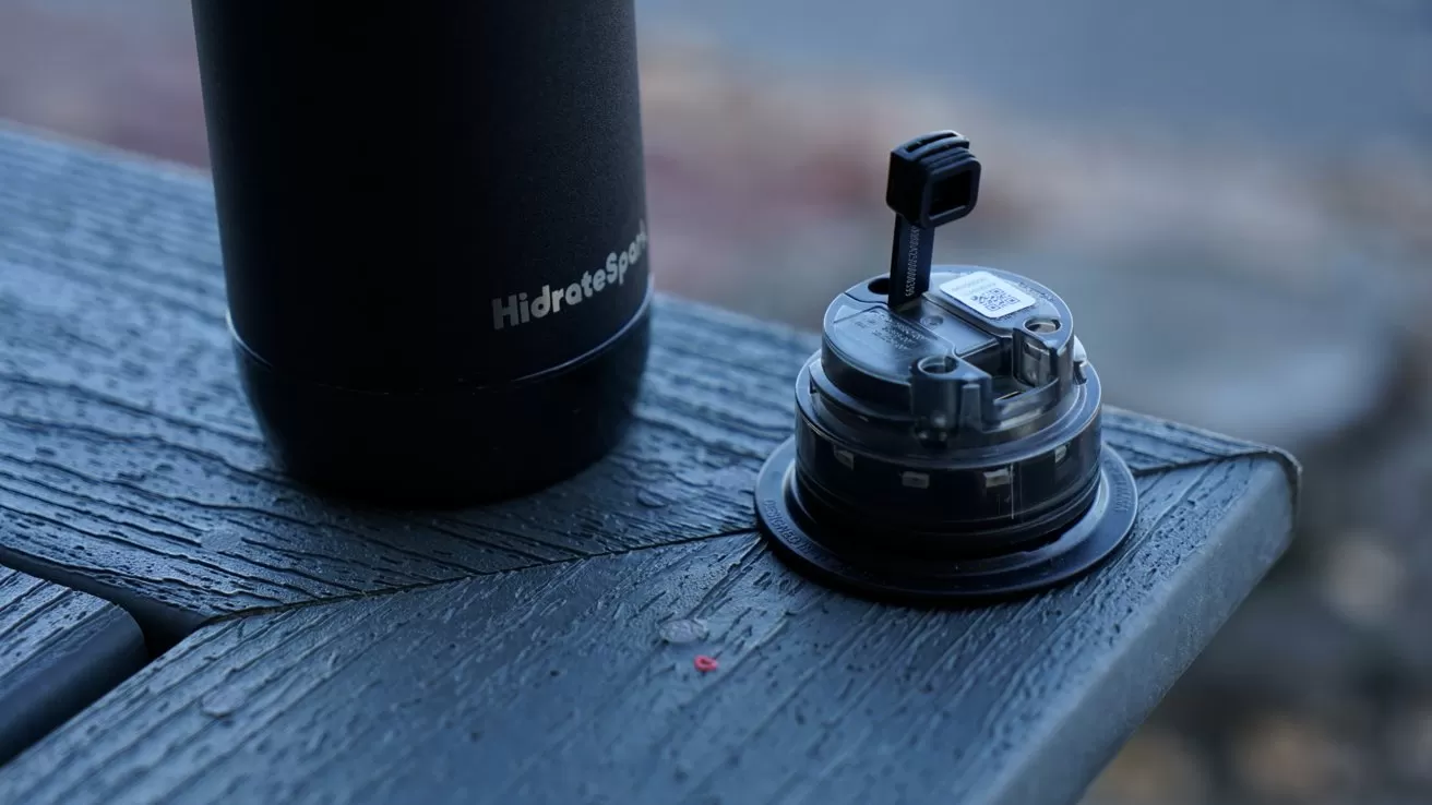 Black insulated water bottle and smart lid on a wet, dark wooden surface.