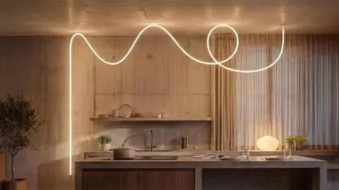 Modern kitchen with warm lighting, featuring a looping neon-style ceiling light above a minimalist island, wooden cabinets, sink, small potted tree, and soft curtains covering a large window