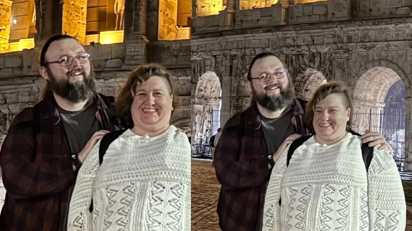 Smiling couple posing together at night in front of an ancient stone amphitheater with arches, warmly lit in the background, man standing slightly behind woman with hands on her shoulders