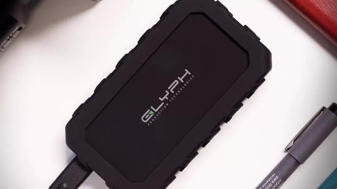 Rugged black Glyph external SSD connected by a cable and resting on a white surface
