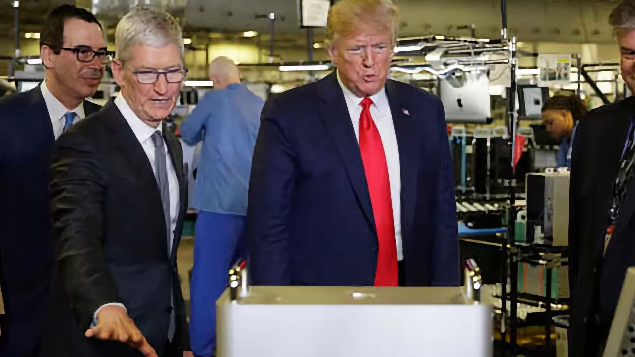 Several men in business suits tour a busy electronics factory, examining a large metallic device while workers and computer equipment appear in the background