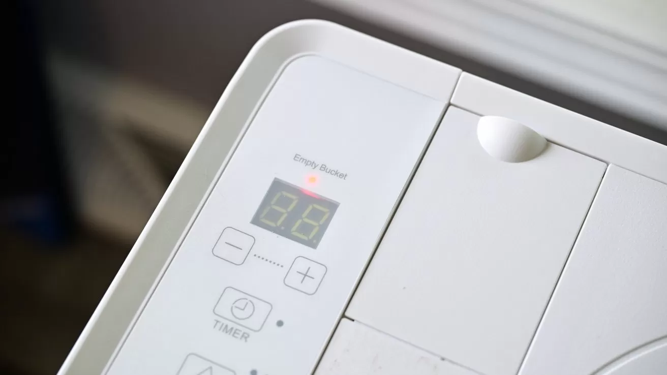 Close-up of a white electronic appliance control panel with digital display reading 89, several buttons including timer controls, a glowing red indicator light, and smooth rounded edges