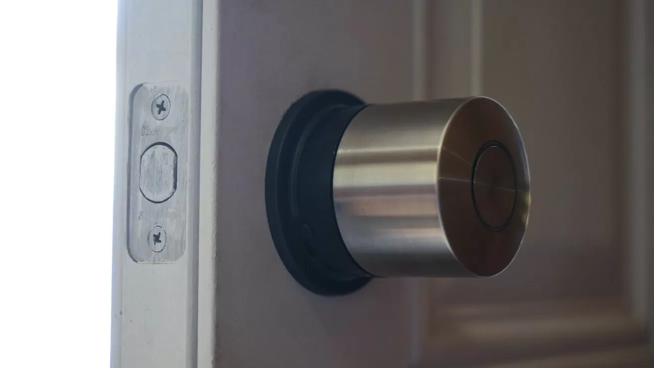 Close-up of a slightly open door showing a modern cylindrical metal doorknob and latch plate, with soft light entering from the left side