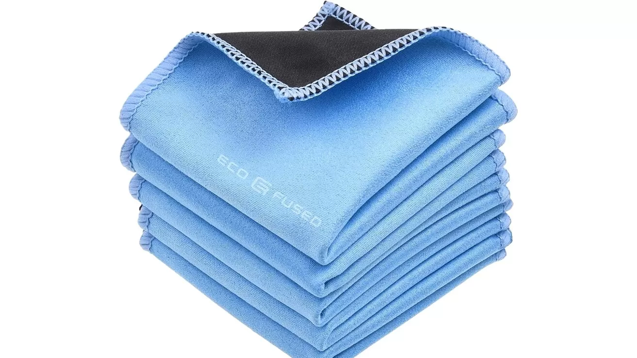 Stack of neatly folded light blue microfiber cleaning cloths with stitched edges, one cloth flipped to show dark underside, arranged on a white background