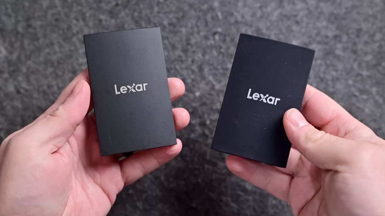 Two hands holding two small black Lexar portable drives against a gray textured background, showing the brand logo centered on each rectangular device