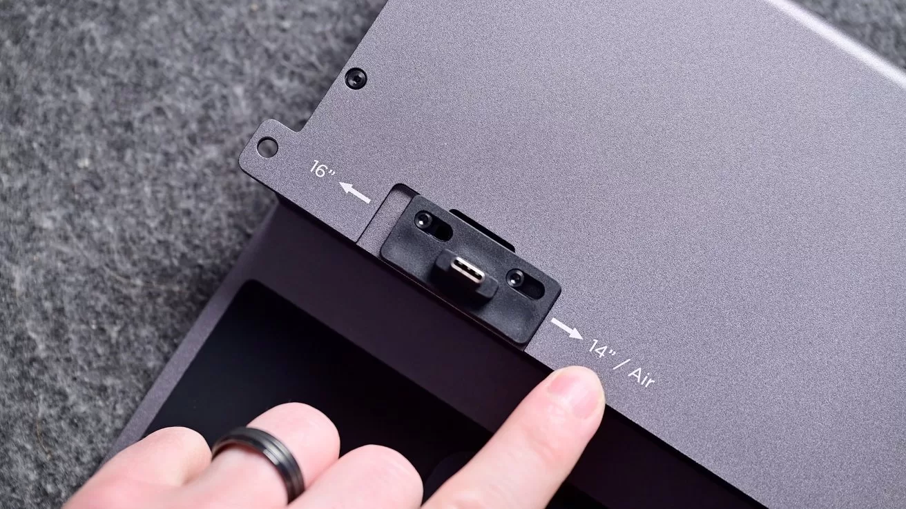 Finger pointing at a small USB-C style connector on a gray metal device, with engraved labels and arrows indicating 16 and 14 / Air size positions on the surface