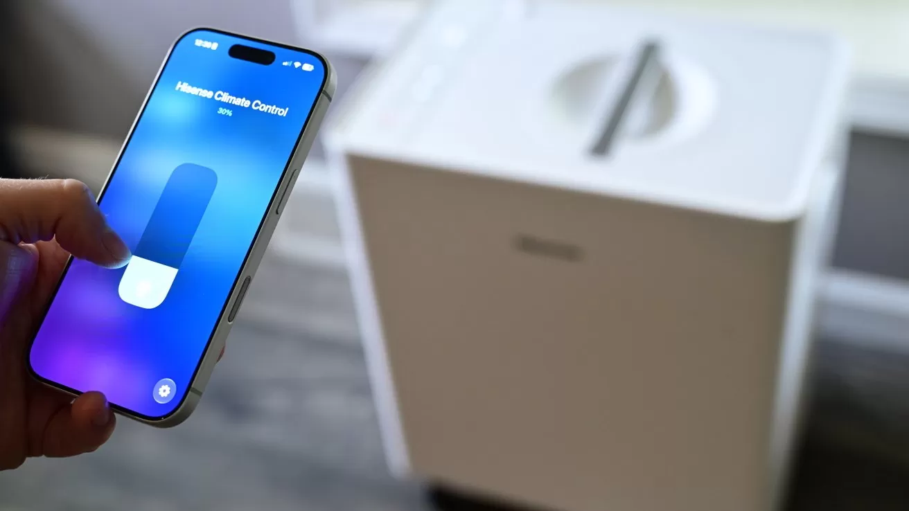 Hand holding a smartphone showing a Home Clean Control slider, positioned near a large white appliance on the floor, suggesting remote control of a home device via mobile app