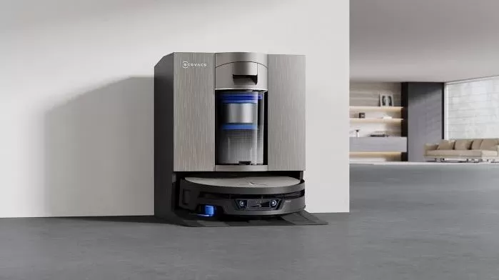 Modern robot vacuum docked in a sleek charging station against a minimalist wall, with a spacious, stylish living area and shelves softly visible in the background