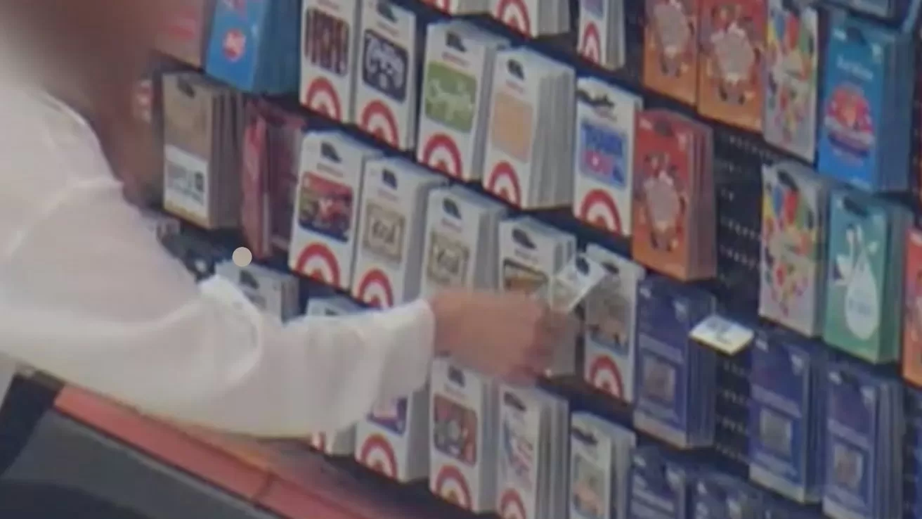 Person reaching toward a store display filled with various colorful gift cards, appearing to select or remove one card from the lower section of the rack