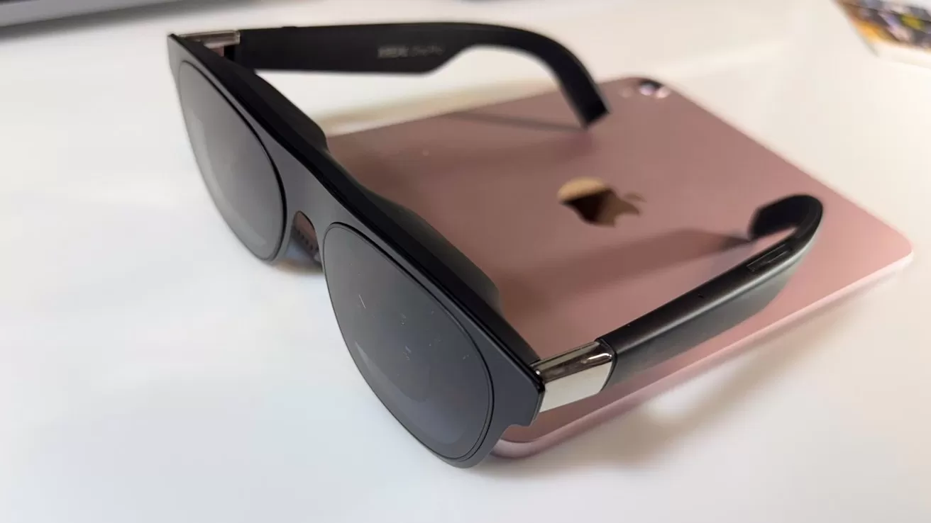 Black sunglasses resting on a rose gold tablet with a partially visible apple logo on a white surface.