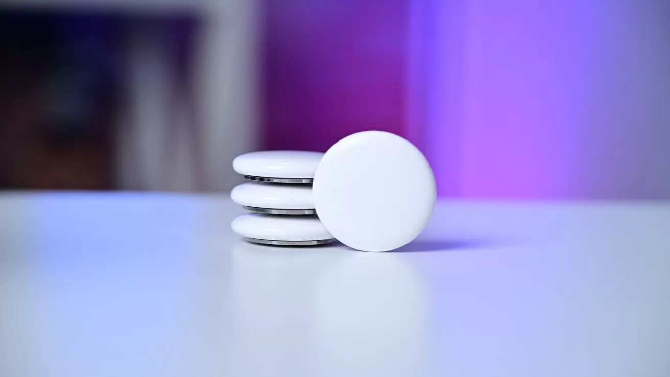 Stack of four round white tracking disks on a smooth light surface, softly lit with purple and blue background tones, emphasizing their clean, minimal tech design