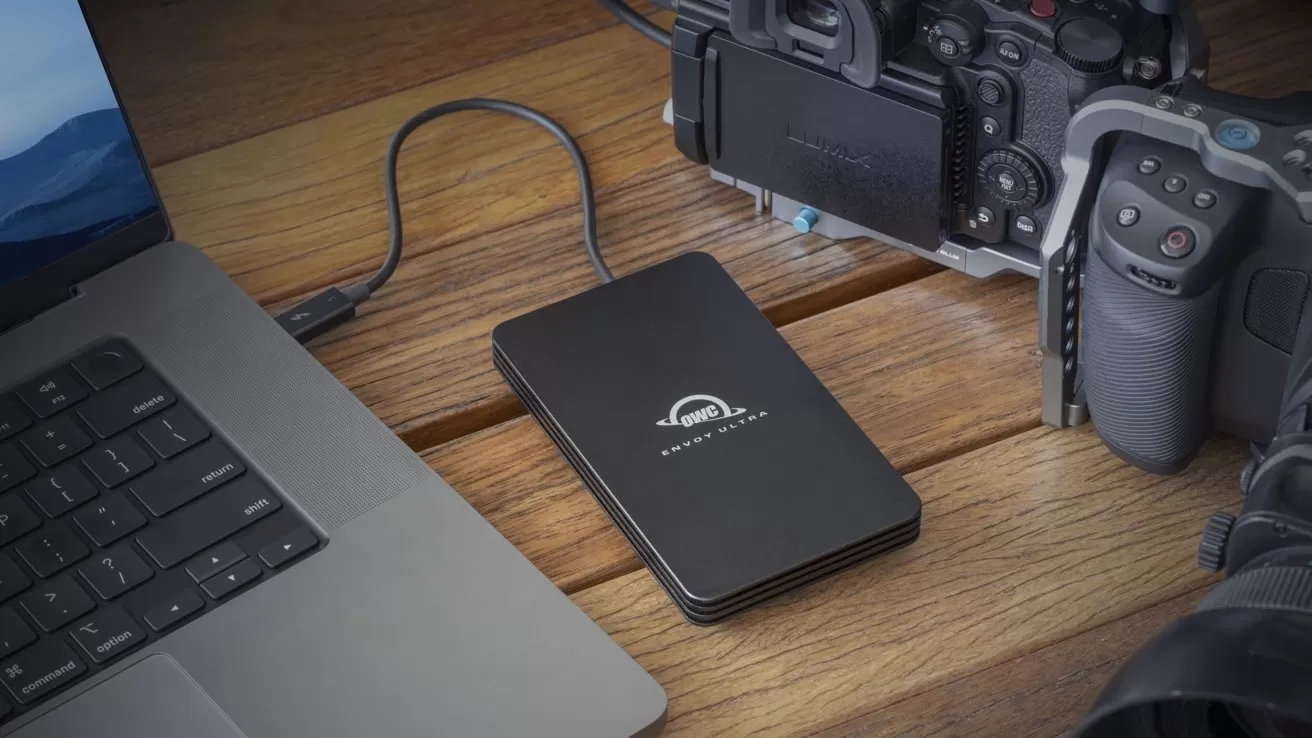External SSD connected to a laptop on a wooden desk, with a professional digital camera and lens nearby