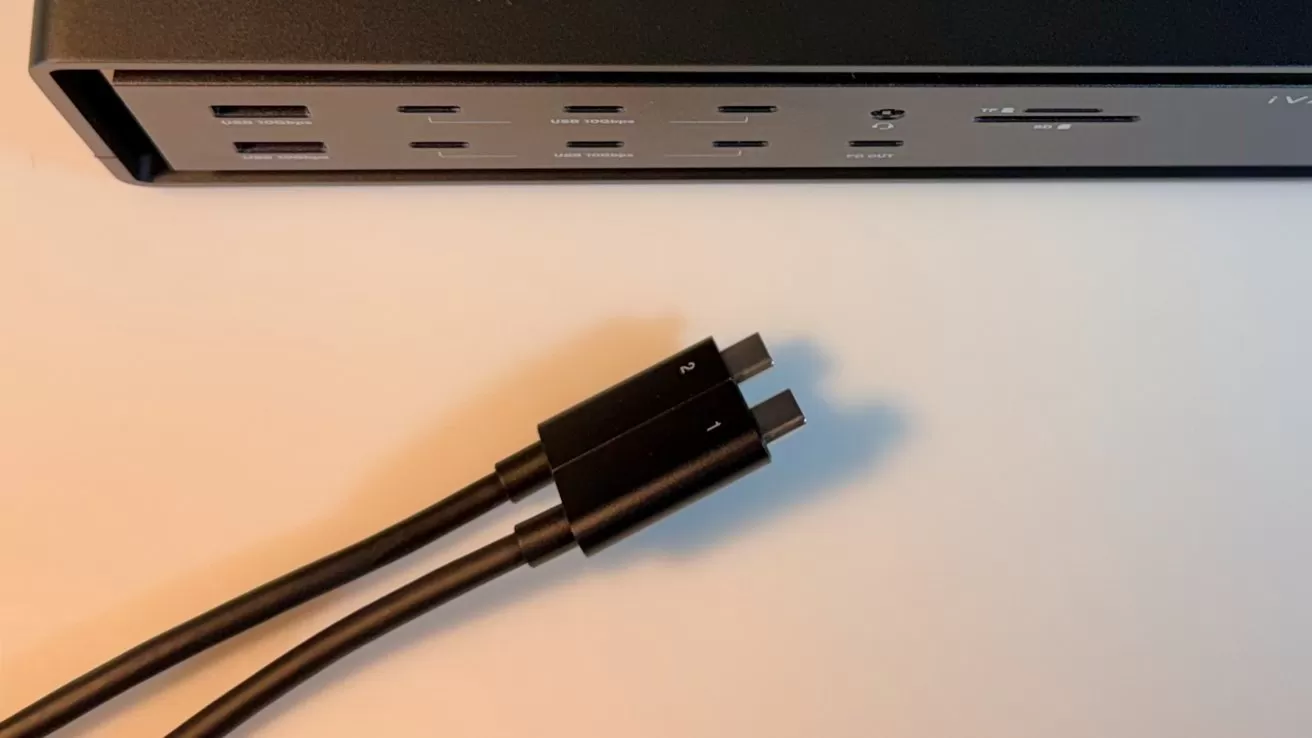 Two black USB-C cables labeled 1 and 2 lying on a white surface in front of a black docking station with multiple USB and memory card slots