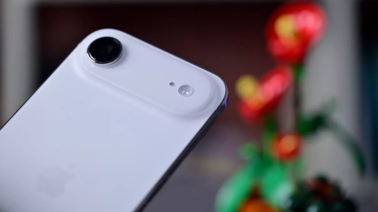 Close-up of a smartphone camera on a white device, with a blurred red and green floral background.