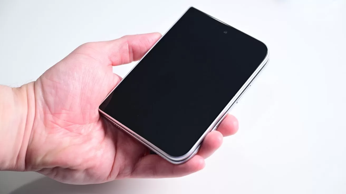 A person's hand holding a closed, black foldable smartphone with rounded corners against a plain white background