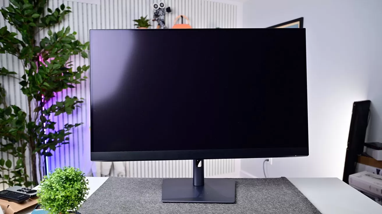 Large black computer monitor on a stand centered on a desk, surrounded by plants, soft ambient lighting, and minimal office decor in a modern, tidy workspace