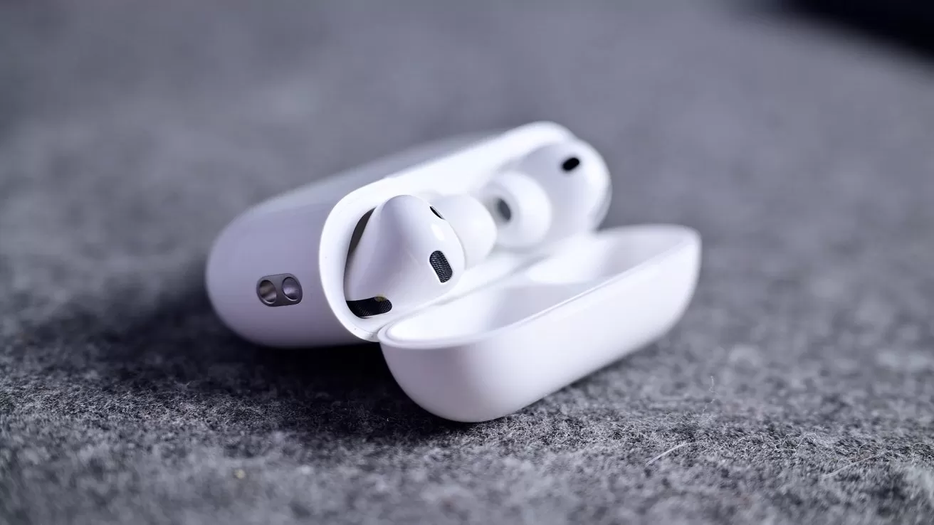 White wireless earbuds resting in an open charging case on a soft gray fabric surface, shown in close-up with emphasis on the sleek, modern design