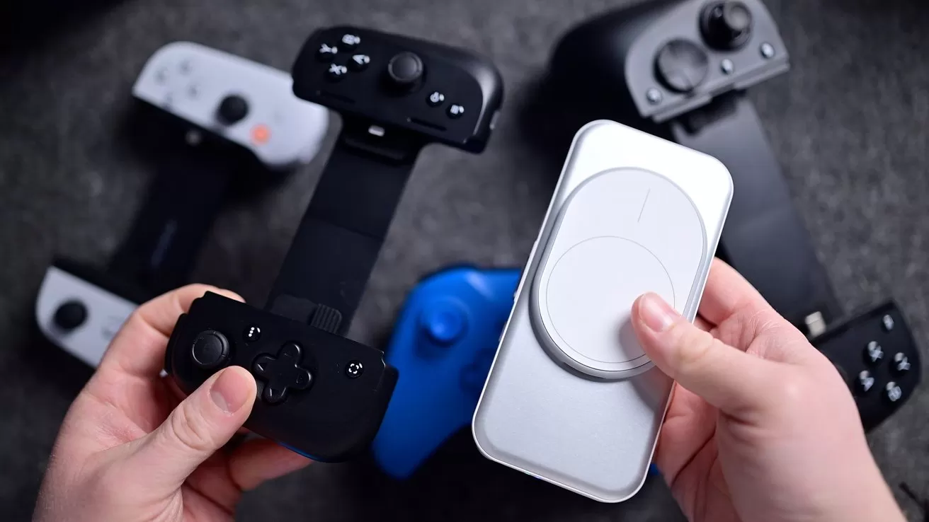 Hands holding a smartphone gaming controller and circular device, with other controllers nearby on a gray surface.