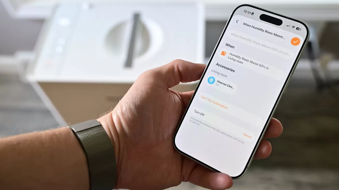 Hand holding a smartphone showing a laundry or washing machine control app, with options and status on the screen, in front of a blurred white front-loading washing machine