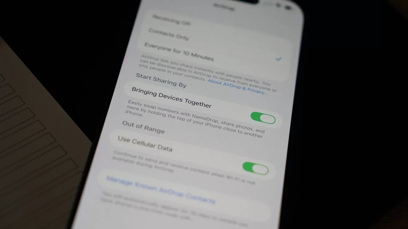 Smartphone screen displaying settings, with options like Bringing Devices Together and Use Cellular Data, shown as green toggles, on a slightly angled phone resting on a dark surface
