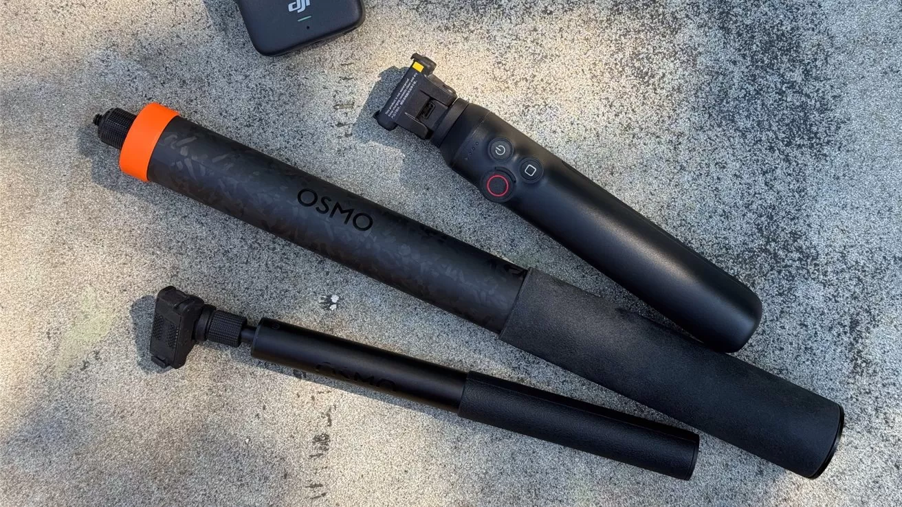 Three black handheld camera accessories on rough concrete: a DJI Osmo grip with control buttons, a long OSMO-branded extension pole with orange end, and a shorter adjustable mounting arm