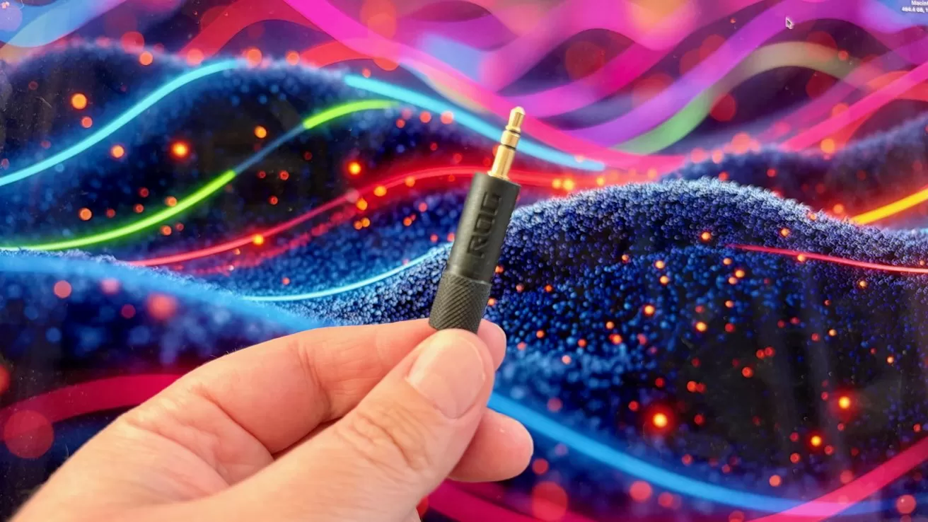 Hand holding a small audio jack plug in front of a colorful abstract background with glowing, wavy lines and sparkling dots, suggesting vibrant digital sound or music visualization