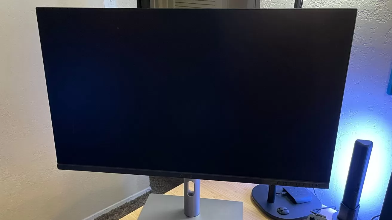 A black computer monitor on a desk, illuminated by blue light, with a remote control nearby.