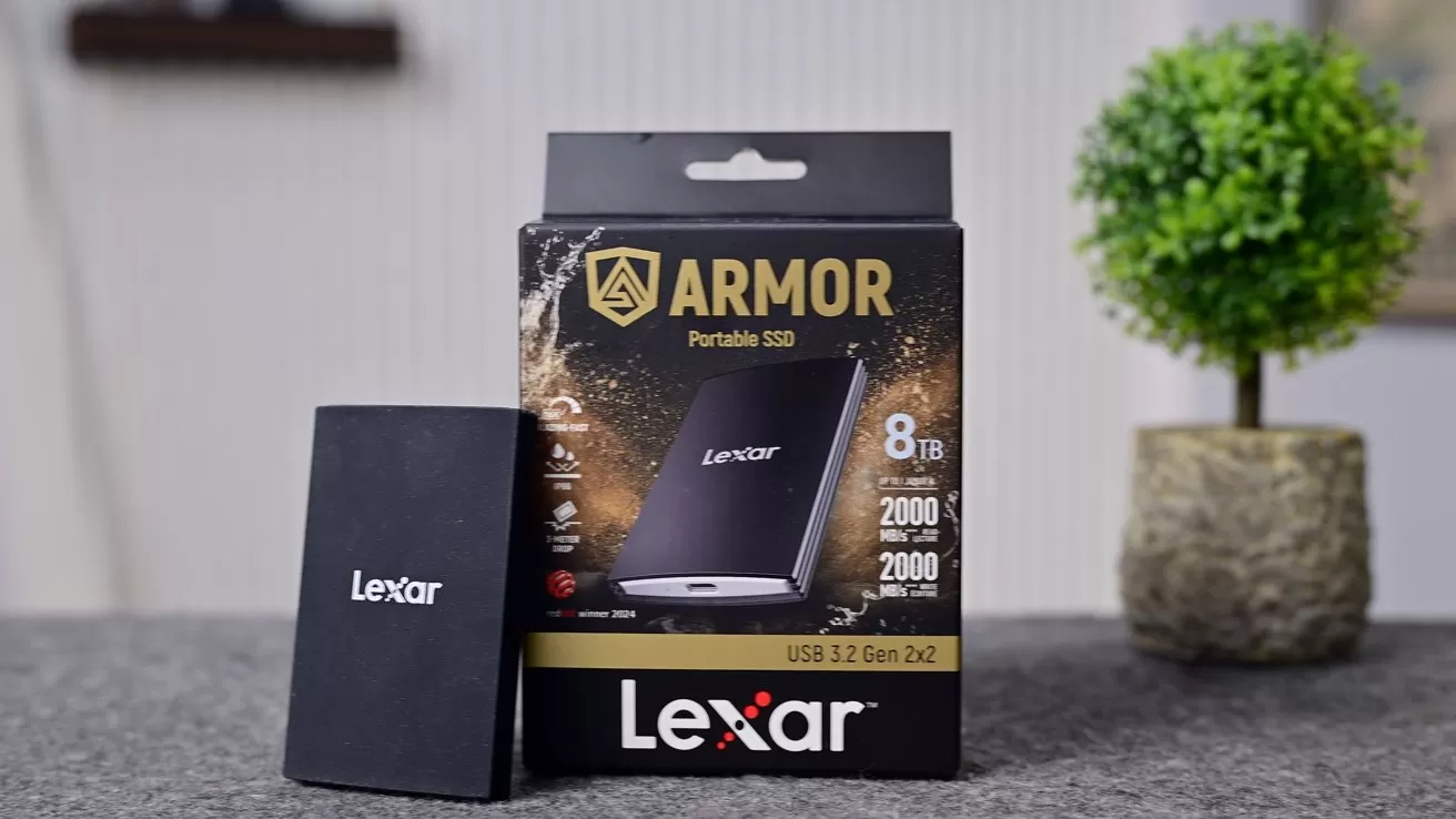 Lexar Armor portable SSD standing beside its retail box on a gray surface, with product capacity details shown; small potted plant blurred in the background indoors