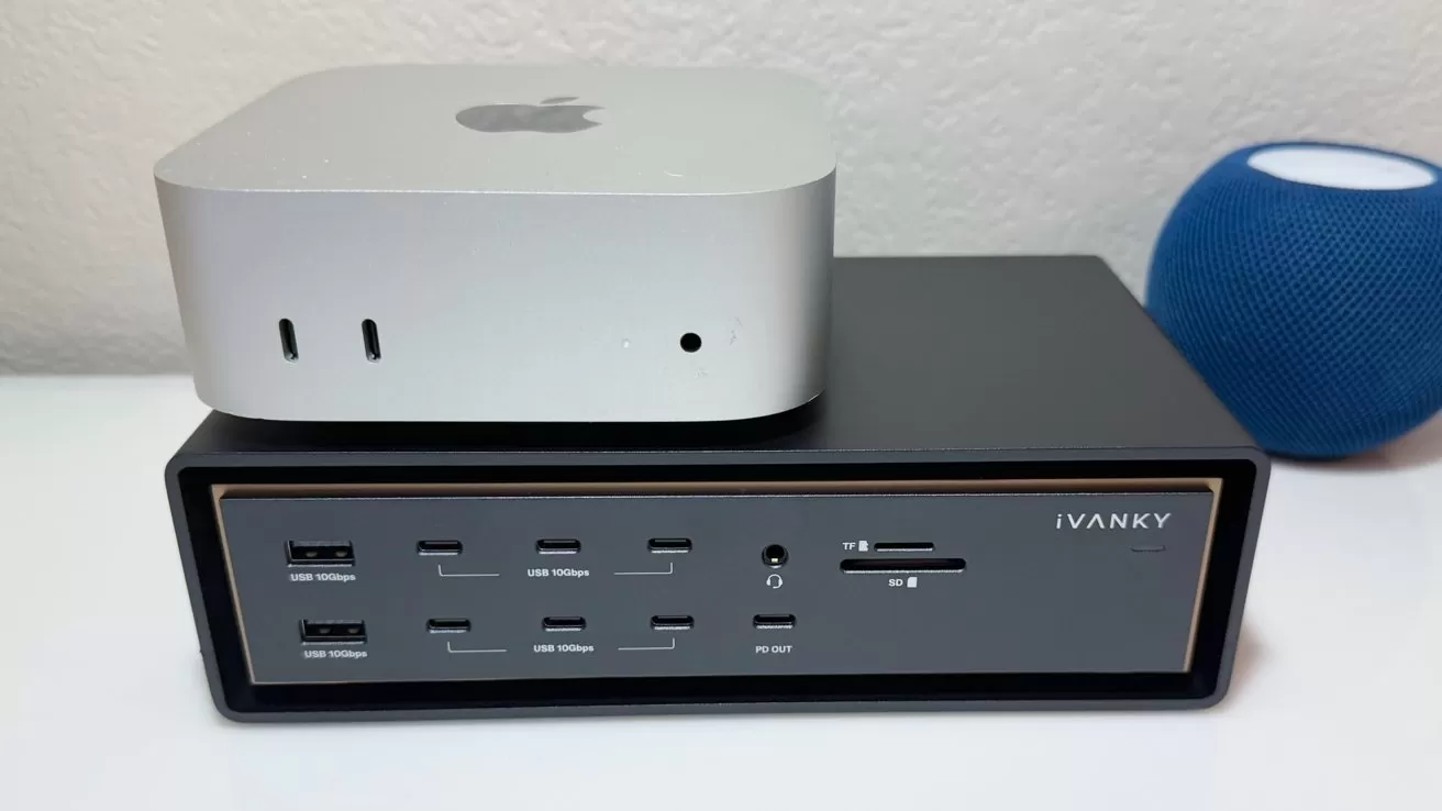 Silver Mac mini computer stacked on a black iVANKY docking station with multiple USB and card ports, sitting on a white desk beside a small blue spherical smart speaker