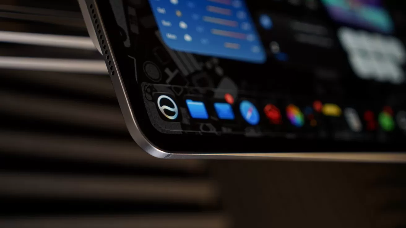 Close-up of a sleek tablet corner showing colorful app icons and widgets on the screen, with a dark blurred background emphasizing the thin metallic edge