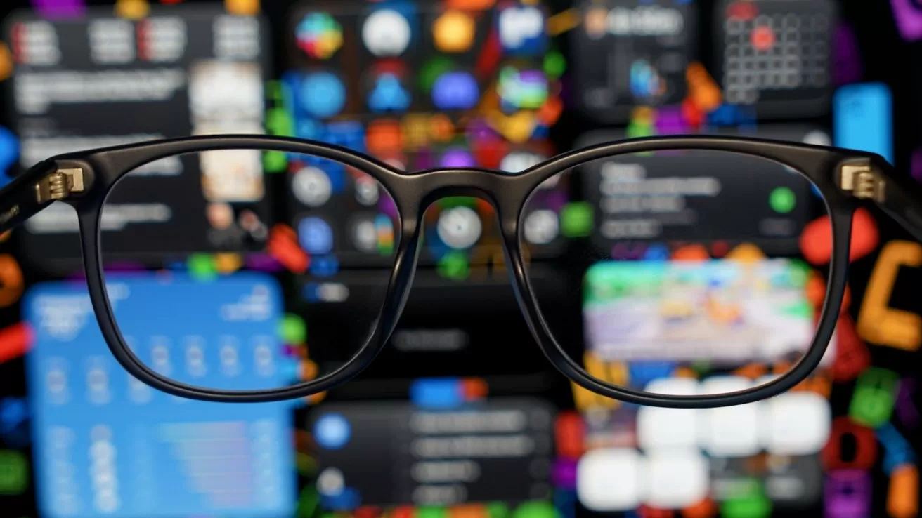 Black eyeglasses in sharp focus against a colorful, blurred background of app icons and digital screens, suggesting technology, notifications, and visual clarity through the lenses