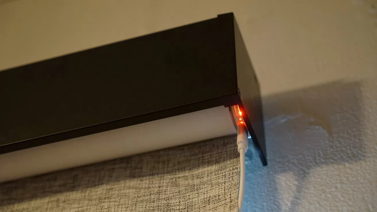 Close-up of a wall-mounted black curtain valance with fabric hanging below and a small red LED light glowing at the corner where a white cable is plugged in