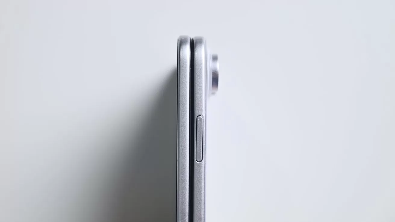 Side view of a closed silver smartphone on a light background, showing its thin profile, side button, and slightly protruding rear camera module