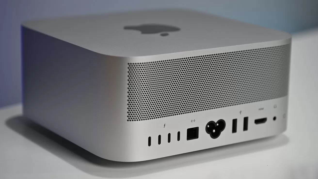 Silver Apple desktop computer with perforated back panel, multiple ports including USB, Thunderbolt, HDMI, Ethernet, and power connector, resting on a white surface against a soft blue background