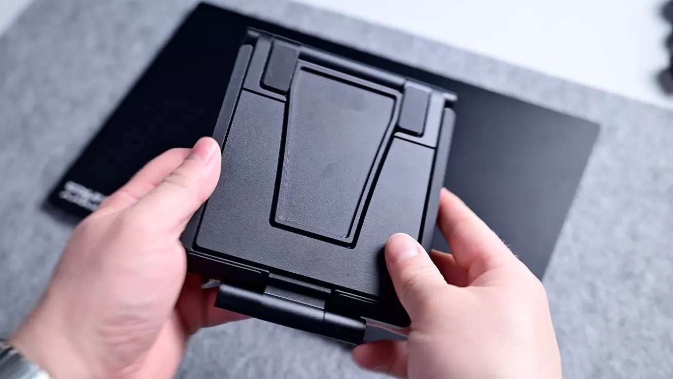 Hands holding a folded black VR headset with a geometric design, against a gray and black background.