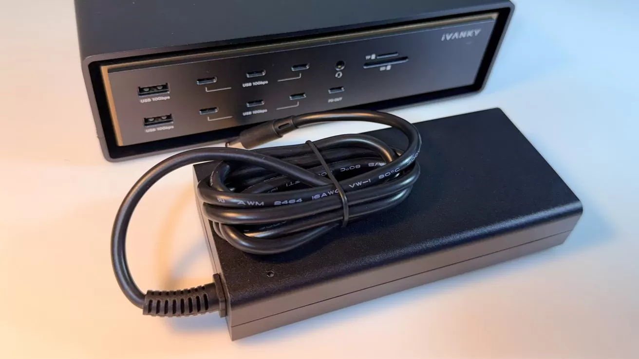 Black IVANKY docking station with multiple USB and card slots, shown behind a large rectangular power brick and coiled power cable resting on a light-colored surface