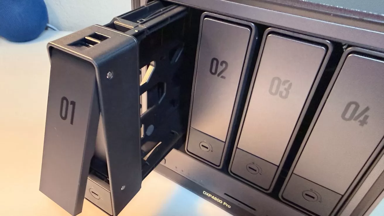 Close-up of a multi-bay network storage device, with drive bay 01 pulled out on a metal tray, and bays 02, 03, and 04 still closed in the enclosure