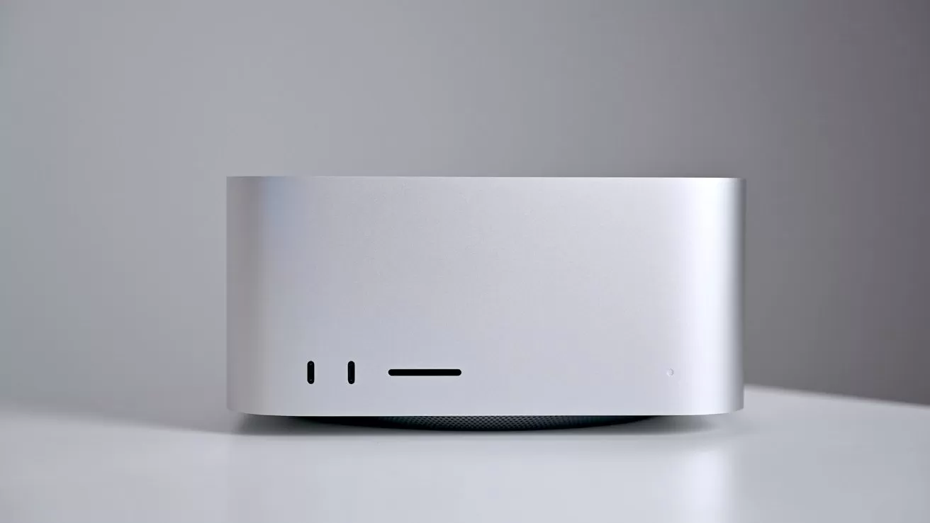 Silver rectangular desktop computer with rounded corners on a white surface against a light gray background, showing front ports and power indicator on the lower left and right sides