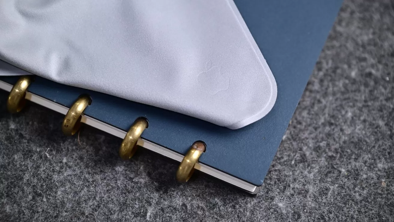 Close-up of a blue notebook with gold metal rings, partially covered by a folded white cloth, resting on a gray textured surface