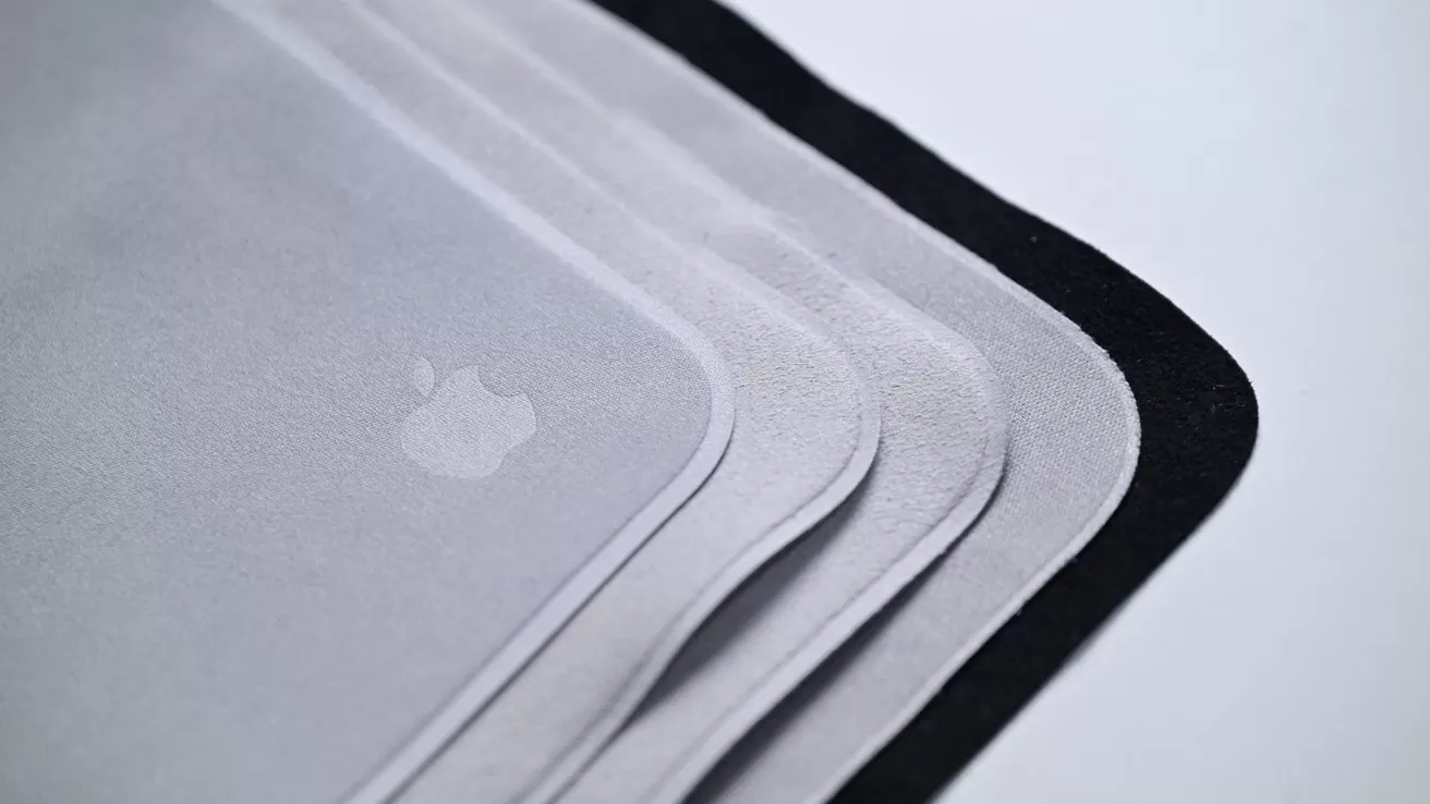 Stacked gray microfiber cleaning cloths with rounded corners and a faint Apple logo, shown close up, overlapping in layers with one darker cloth underneath