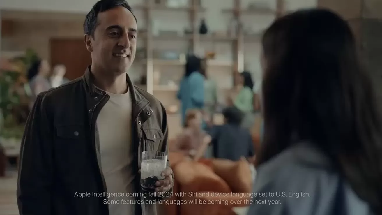 Man holding a drink smiles and talks with a woman in a modern, softly lit lounge area, with relaxed people conversing and sitting on couches in the blurred background
