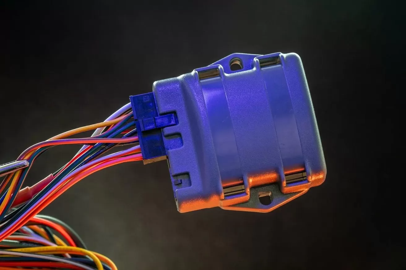 Close-up of a cylindrical electronic connector with a bundle of multicolored wires attached, lit with blue and orange highlights against a dark, blurred background